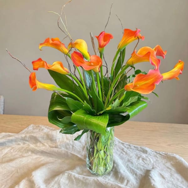 Orange and yellow calla lilies in a clear glass vase