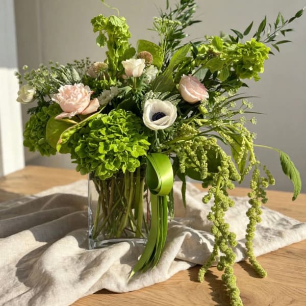 Green and blush floral arrangement in a clear glass vase