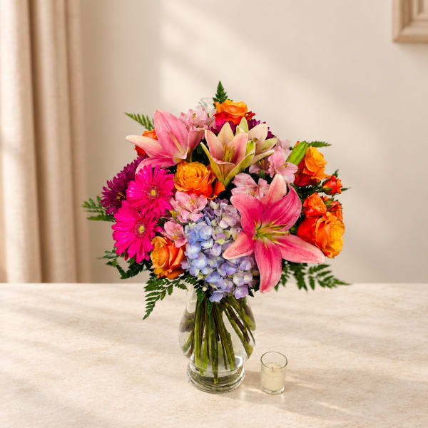 Colorful bouquet of lilies, roses, gerbera daisies, and hydrangeas in a glass vase