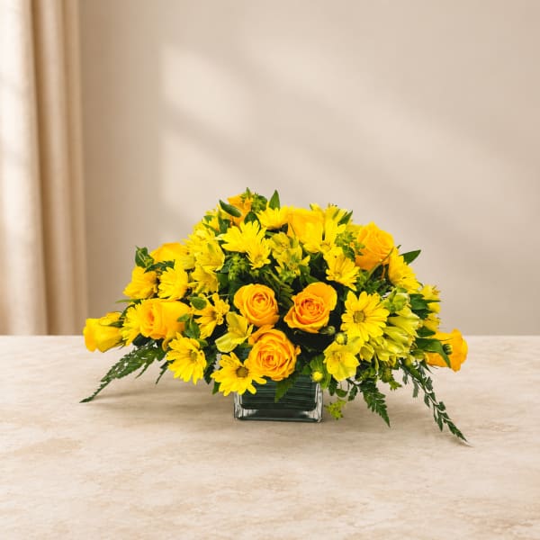Yellow roses and daisies arranged in a square glass vase