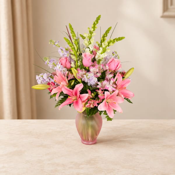 Pink lilies and roses arranged in a frosted glass vase
