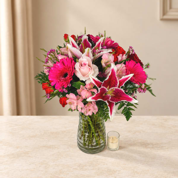 Pink and red mixed bouquet in a glass vase with a small candle beside it