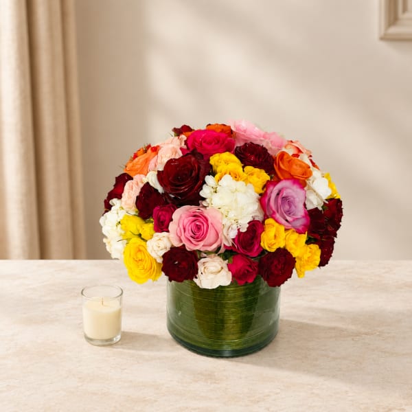 Colorful rose bouquet in a green glass vase with a small candle beside it