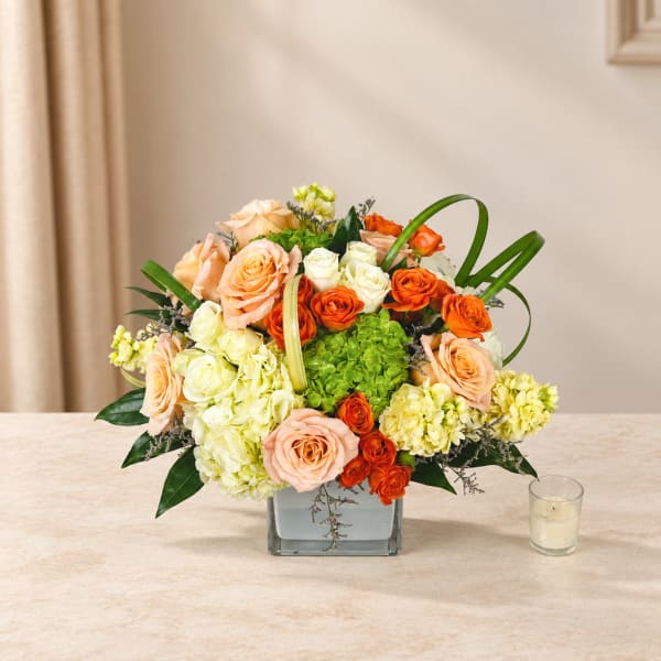 Peach and orange roses with pale hydrangeas in a square glass vase