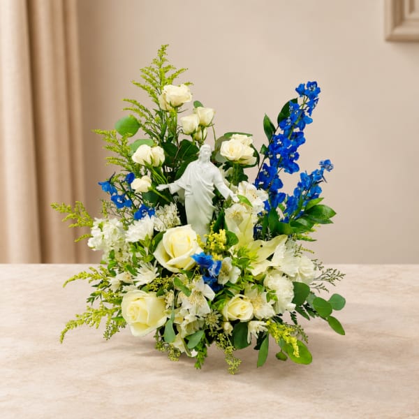 White roses and blue flowers arranged around a small statue in a vase