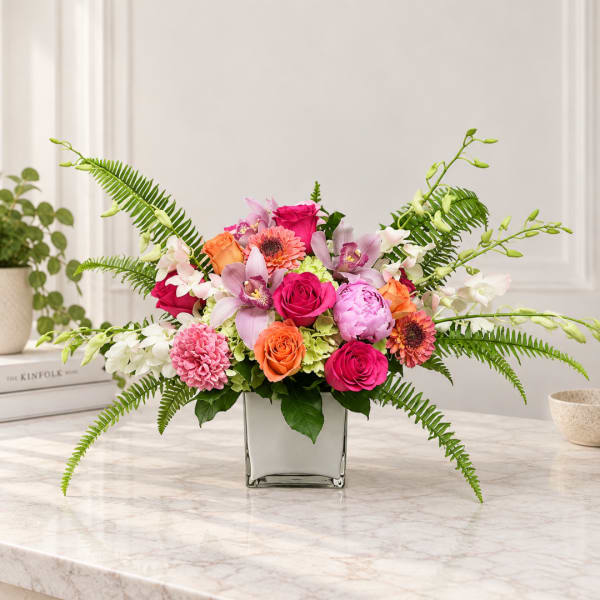 Mixed pink and orange flowers arranged in a square glass vase