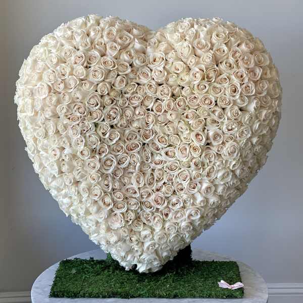 Heart-shaped arrangement of cream roses on a green base