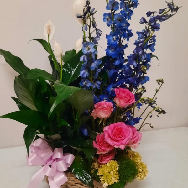 Pink roses and blue delphinium in a basket with a pink ribbon