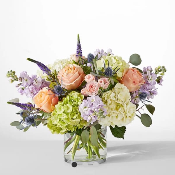 Mixed bouquet of peach roses, hydrangeas, and purple flowers in a glass vase