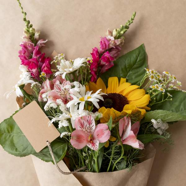 Bouquet of sunflowers, pink alstroemeria, and white daisies in kraft paper