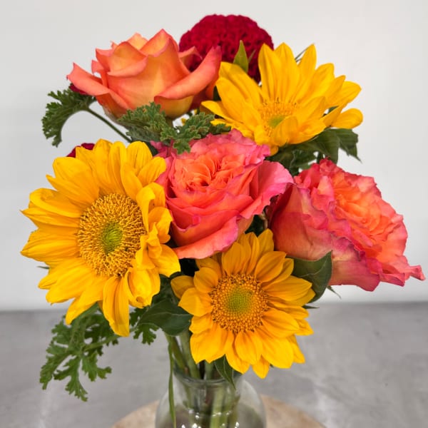 Bouquet of orange roses and yellow sunflowers in a clear glass vase