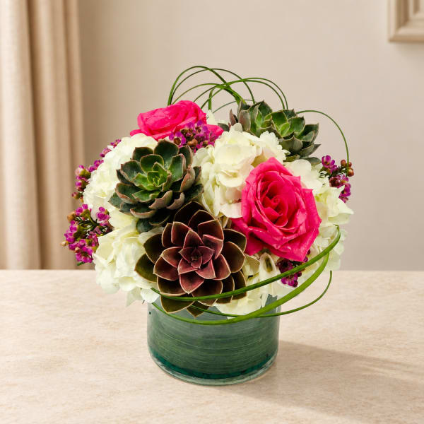 Pink roses and white hydrangeas arranged with succulents in a glass vase