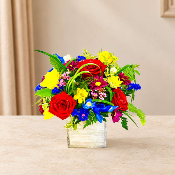 Colorful bouquet of roses and mixed flowers in a clear square vase