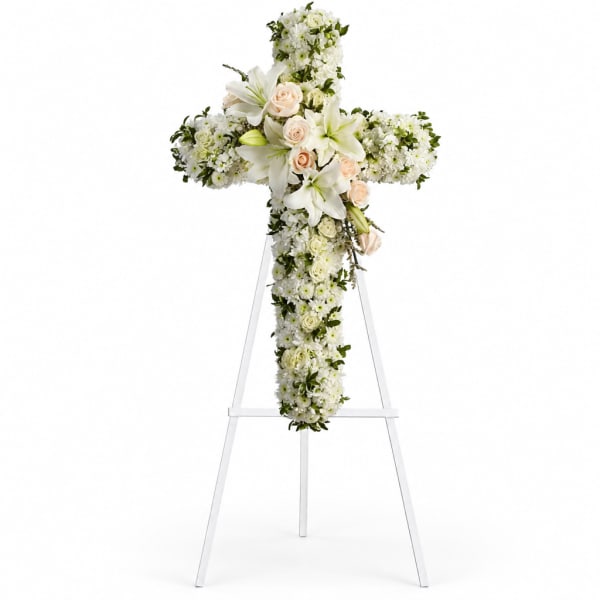 White floral cross on a stand with pale roses and lilies