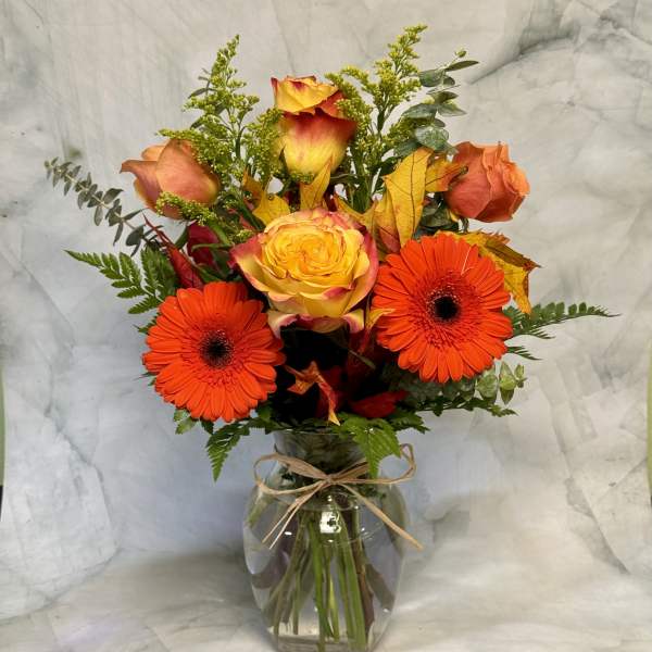 Bouquet of orange gerbera daisies and yellow-orange roses in a glass vase