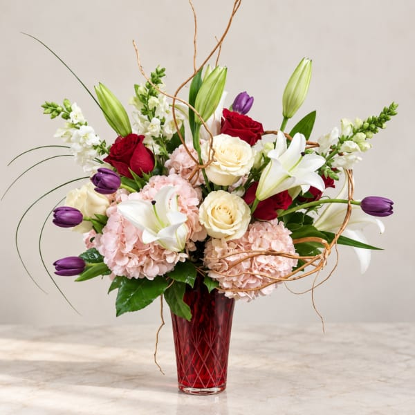 Mixed bouquet of roses, lilies, hydrangeas, and tulips in a red vase