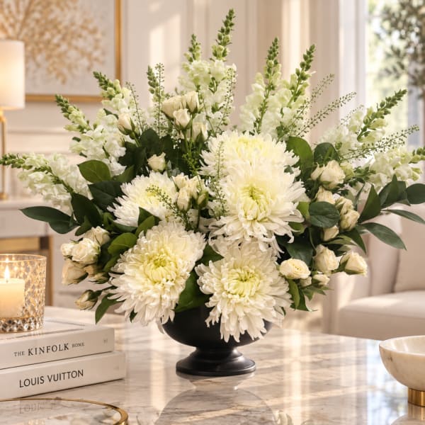 White floral arrangement in a black pedestal vase on a table