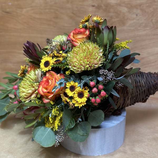 Mixed bouquet with orange roses, yellow blooms, and dark foliage in a wicker cone