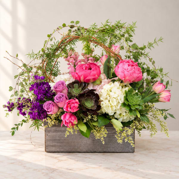 Mixed pink and purple flowers arranged in a wooden box with greenery