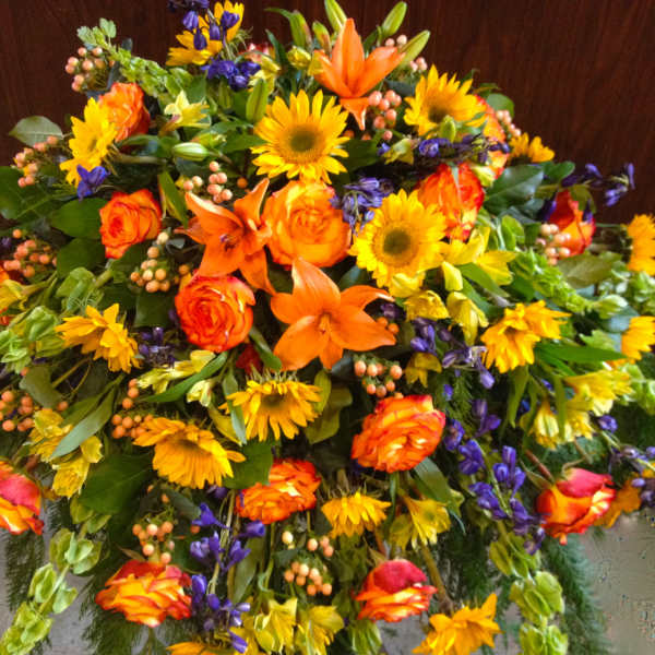Large mixed floral spray with orange roses, lilies, and yellow sunflowers
