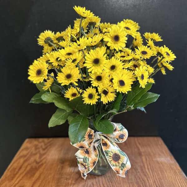 Yellow daisy bouquet in a glass vase with a sunflower-patterned ribbon