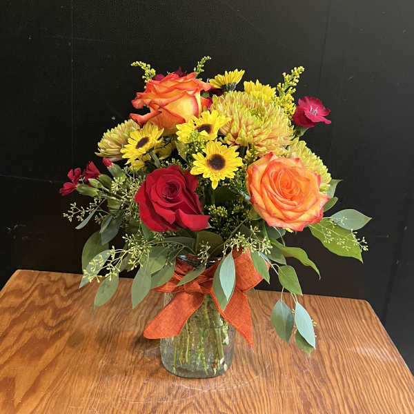 Bouquet of orange and red roses with yellow daisies in a glass vase