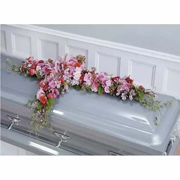 Pink and red floral cross spray displayed on top of a closed gray casket.