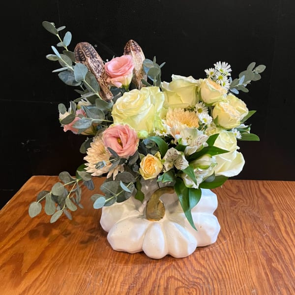 Floral arrangement in a white pumpkin-shaped vase with pink and cream blooms
