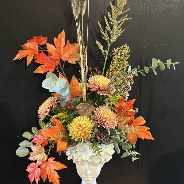 Autumn floral arrangement in a white vase with orange leaves and chrysanthemums