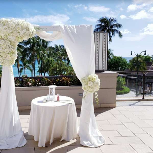 White floral wedding arch with draped fabric and a small round table
