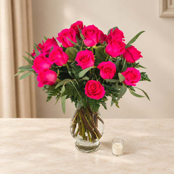 Hot pink roses arranged in a clear glass vase with greenery