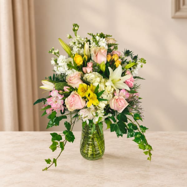 Mixed bouquet of lilies, roses, and white blooms in a glass vase