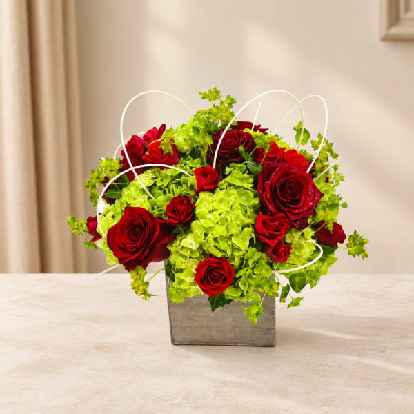 Red roses and green hydrangeas in a square gray vase with white loops