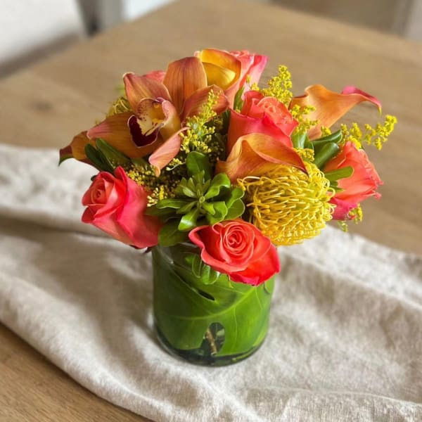 Pink roses and orange orchids in a glass vase with yellow filler flowers