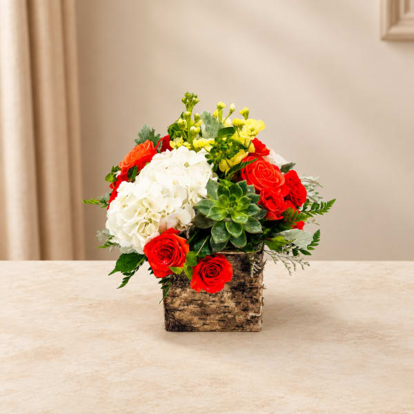 Mixed bouquet of red roses, white hydrangea, and yellow flowers in a rustic box