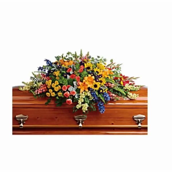 Colorful mixed flower casket spray with yellow, orange, blue, and pink blooms on a wooden casket