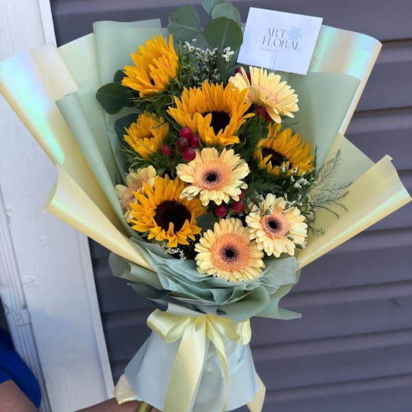 Bouquet of sunflowers and pale gerbera daisies wrapped in pastel paper
