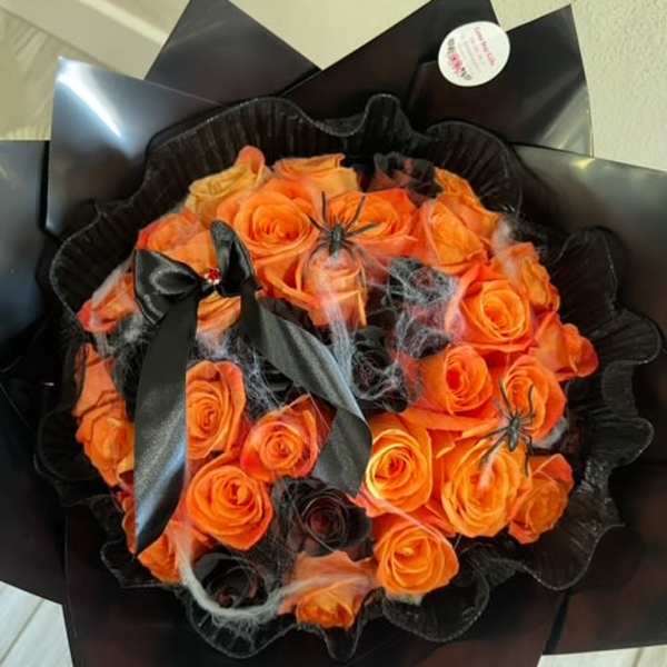 Orange rose bouquet wrapped in black paper with ribbon and spider decorations