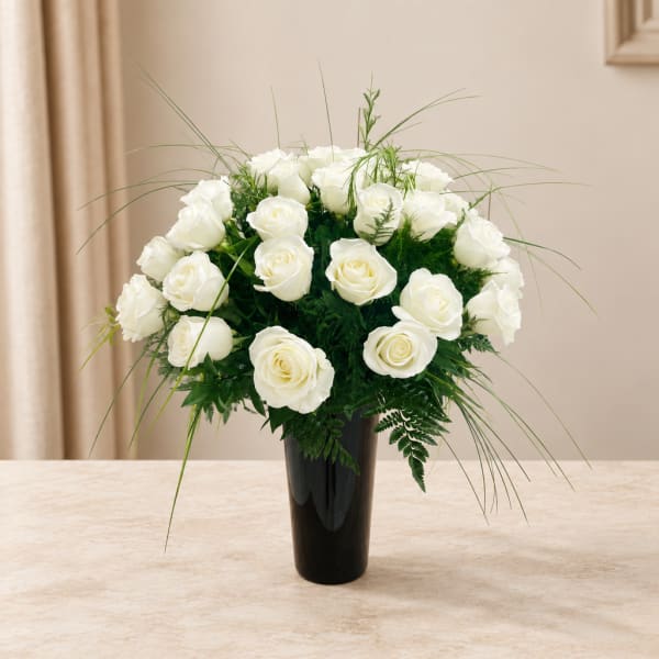White roses arranged in a black vase with airy greenery