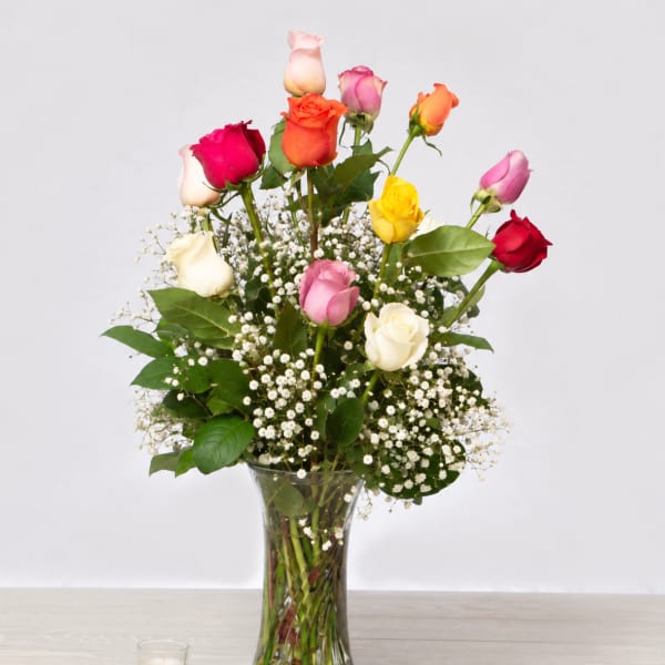 Mixed roses in a clear glass vase with baby's breath and a candle nearby