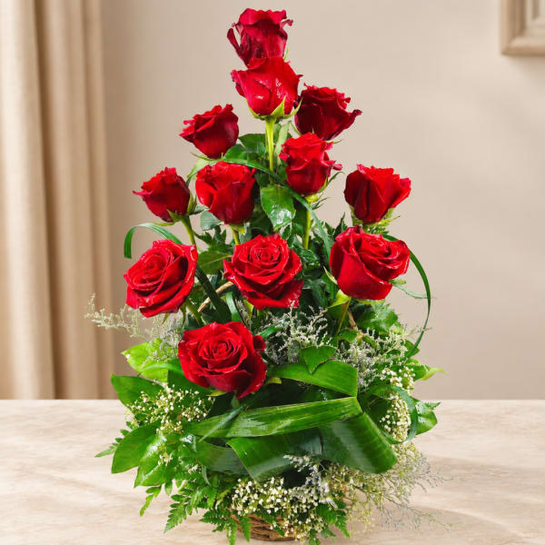 Red roses arranged in a basket with greenery