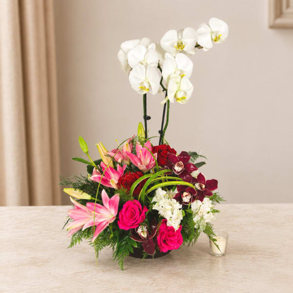 Mixed bouquet with white orchids, pink lilies, and red roses in a low container