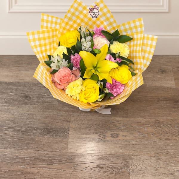 Bouquet of yellow, pink, and white flowers wrapped in yellow checkered paper