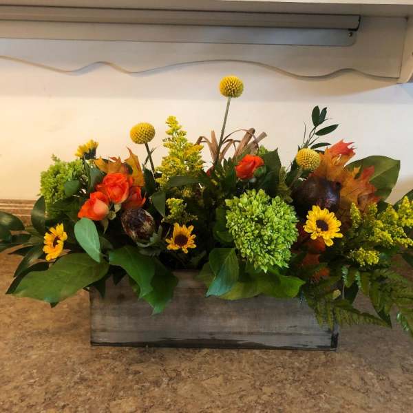 Low floral arrangement with orange roses, yellow blooms, and green hydrangea in a wooden box