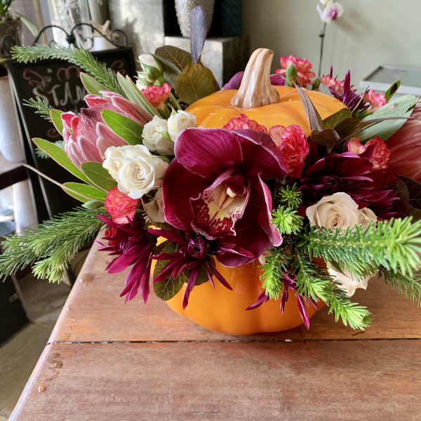 Floral arrangement in a pumpkin-shaped container with burgundy and white blooms