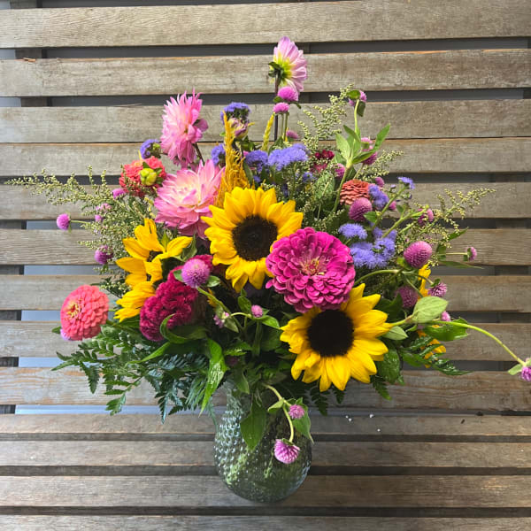 Colorful mixed bouquet with sunflowers, zinnias, and purple blooms in a glass vase