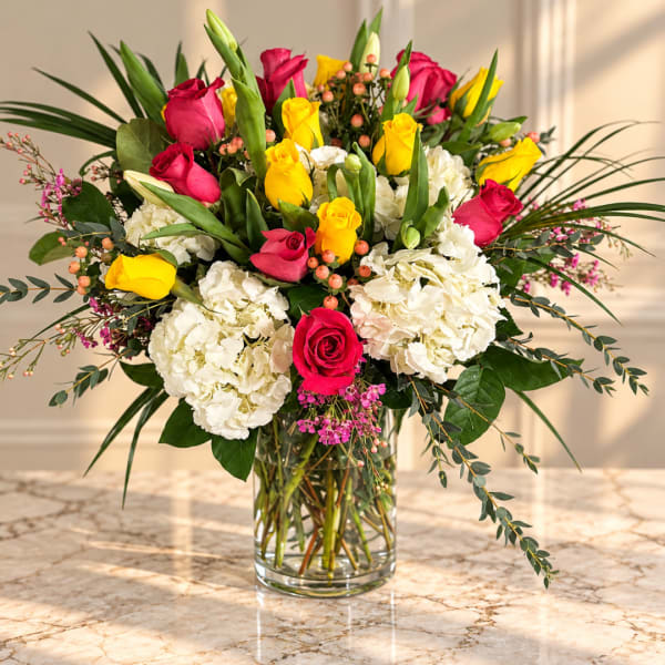 Bouquet of pink and yellow roses with white hydrangeas in a clear glass vase