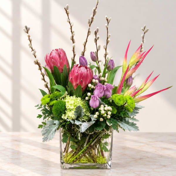 Colorful floral arrangement in a clear square vase with pink, purple, and green blooms