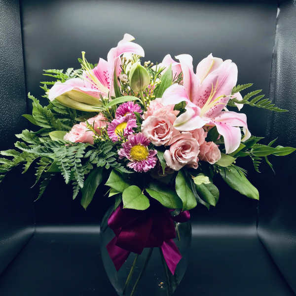 Pink lilies and roses in a glass vase with a magenta ribbon