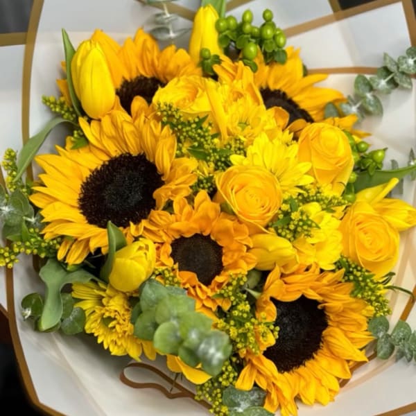 Yellow sunflowers and roses arranged in white paper with green accents.